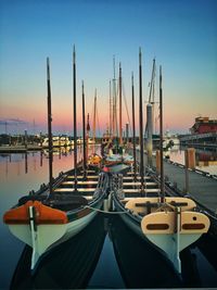 Boats moored in harbor at sunset