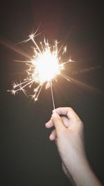 Cropped hand of woman holding lit sparkler at night