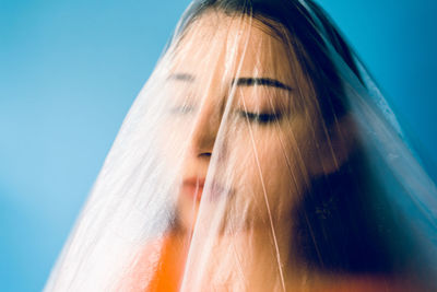 Teenage girl wrapped in plastic against blue background