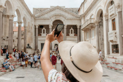 Rear view of woman taking a photo in a busy city square at diocletian's palace in split, croatia