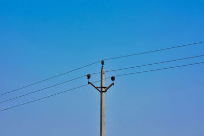 Low angle view of electricity pylon against blue sky