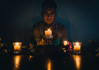 Portrait of young man sitting with candles in darkroom