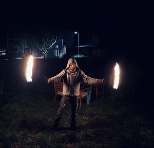 Man standing by illuminated fire at night