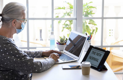 Senior woman wearing mask using laptop at home