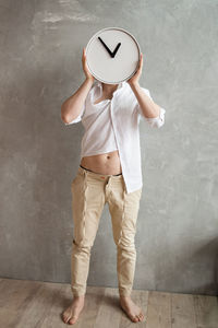 Man in white shirt holds round white clock covering his face.