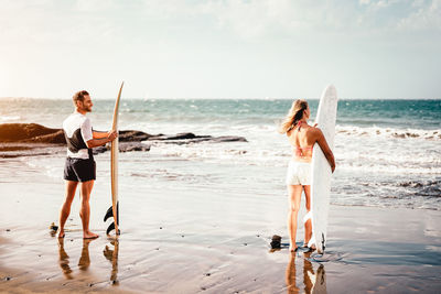 Man and woman holding surfboards while standing at beach against sky