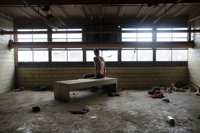 Rear view of shirtless man sitting in abandoned room