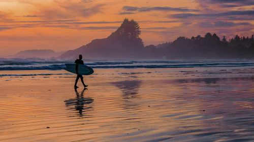 Silhouette woman walking at beach against sky during sunset