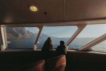 Rear view of man and woman leaning by window in boat