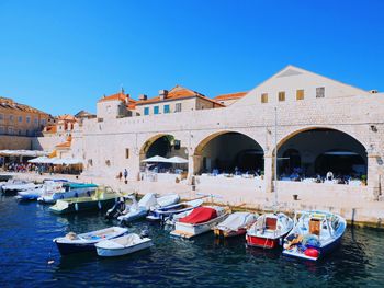 Boats moored in canal by buildings against clear blue sky