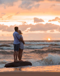 Rear view of couple on beach against sky during sunset