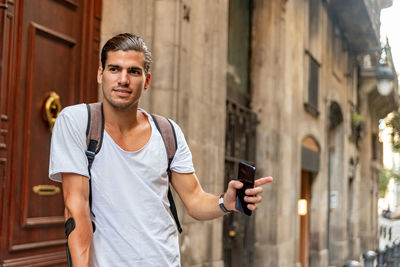 Young tourist holding mobile phone while standing outdoors