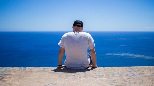 Rear view of man sitting against sea against clear sky