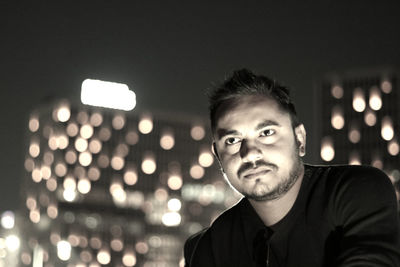 Young man looking away against illuminated building at night