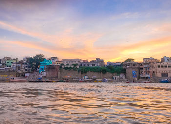 Buildings by sea against sky during sunset