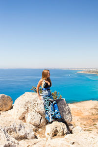 Man sitting on rock by sea against clear sky