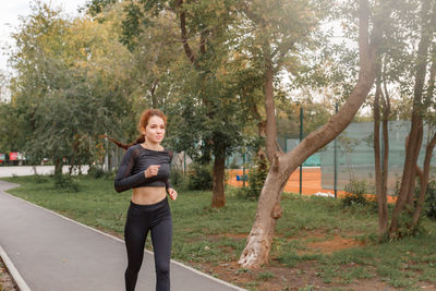 Young attractive girl in sports tight clothes running in the park among green foliage