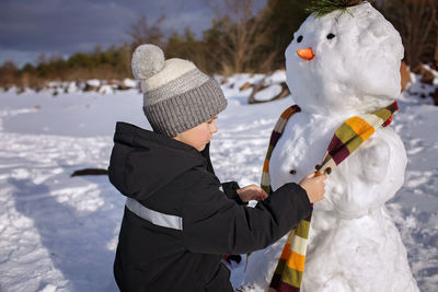 Boy in hat makes snowman, which was the nose of snowman, smiling. winter family weekend, lifestyle