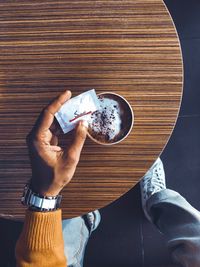 Low section of man holding drink on table