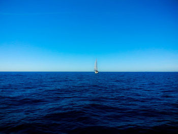 Sailboat sailing in sea against clear blue sky