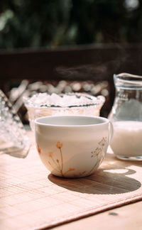 A cup of coffee stands outside on a table next to a jug of milk and a sugar bowl with lump sugar 