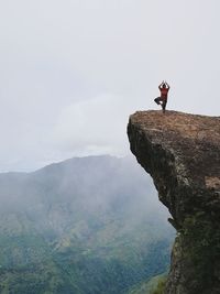 Woman doing tree pose while standing on cliff against sky