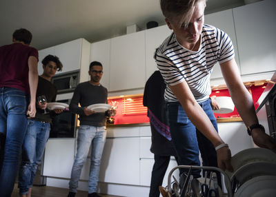 Low angle view of teenage boy arranging plates in dishwasher after dinner party