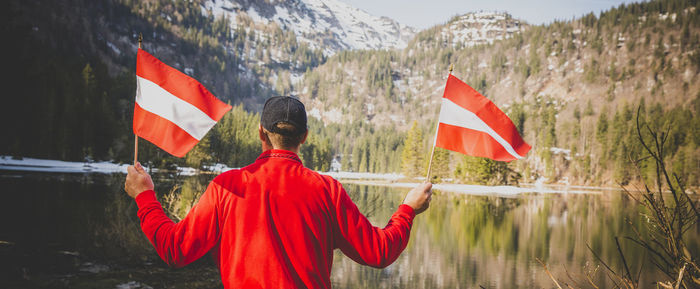 Rear view of man holding flags while standing by lake