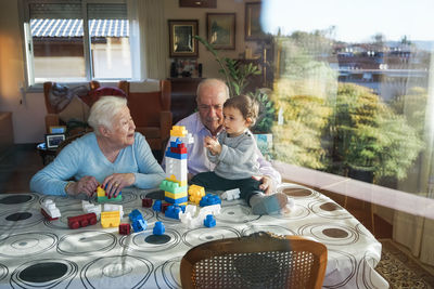 Great-grandparents and baby girl playing together with plastic building bricks at home