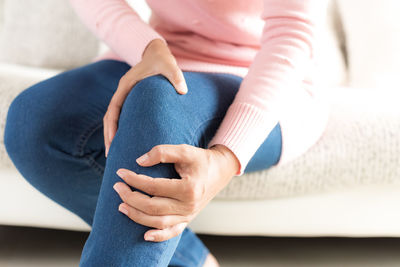 Midsection of woman suffering from knee pain while sitting at home