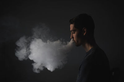 Profile view of young man smoking against gray background