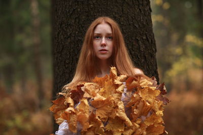 Portrait of young woman covered with leaves at forest during autumn