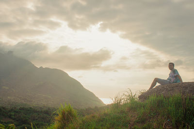 Man sitting on mountain against sky