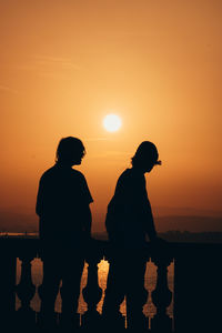 Silhouette people standing by sea against orange sky