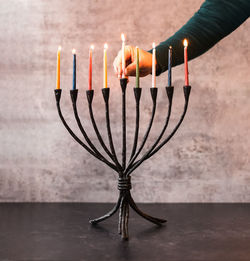 Woman's hand placing a lit candle in a menorah for hanukkah.