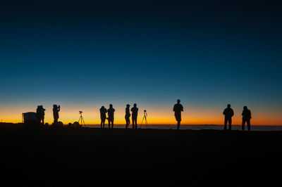 Silhouette people on land against sky during sunset