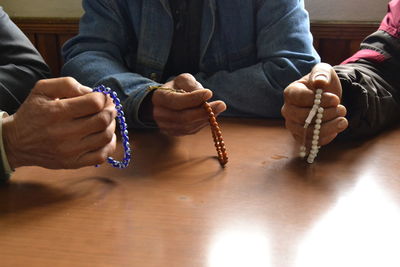Midsection of people chanting using beads at wooden table