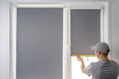 Rear view of man holding window at home