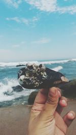 Close-up of hand holding sea against sky