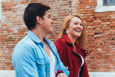 Portrait of smiling young couple standing against brick wall