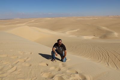 Full length of man kneeling on sand dune in desert