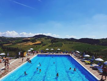 People swimming in pool against blue sky