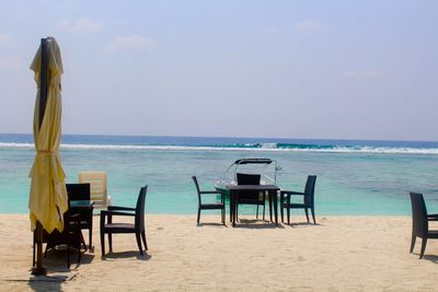 Empty chairs on beach against sky