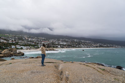 Woman standing on rock by sea against sky