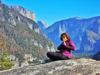 Woman sitting on rock against mountains