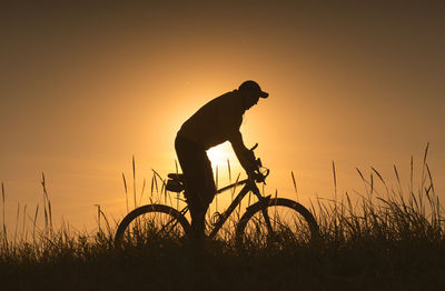 Silhouette man with bicycle on field against sky during sunset