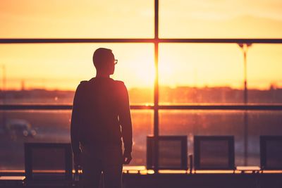 Rear view of silhouette woman standing by railing against river during sunset