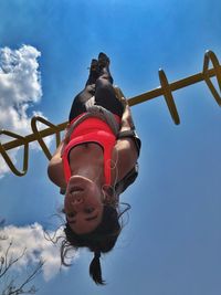 Low angle view of mid adult woman hanging upside down on monkey bars against blue sky during sunny day