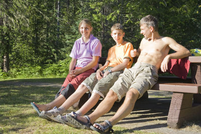 Portrait of children with father sitting on bench in forest