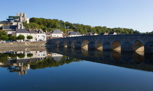 Arch bridge over river by buildings against sky